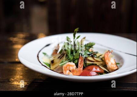 Frischer Fisch Salat mit Garnelen, Arugula, Käse und Tomaten in der Schüssel auf rustikalem Holzhintergrund Stockfoto