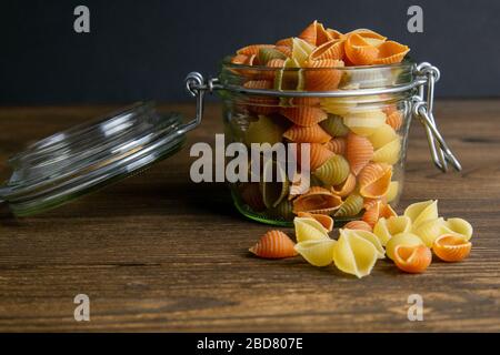 Bunte Conchiglie Pasta im Glasbecher auf Holzhintergrund. Vorderansichten, Nahaufnahme Stockfoto