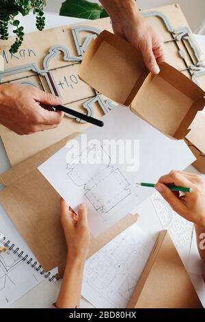 Boxhersteller, die hinter einem Tisch arbeiten und die Schaltpläne eines Kastens besprechen Stockfoto