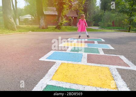 Kleines Mädchen in einem rosa Kleid spielen hopscotch auf Spielplatz im Freien, Kinder Aktivitäten im Freien Stockfoto