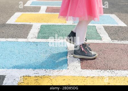 Nahaufnahme der Beine des Mädchens in einem rosa Kleid und hopscotch auf Asphalt gezogen. Kind spielt Hopscotch auf Spielplatz im Freien an einem sonnigen Tag. Im Freien Stockfoto