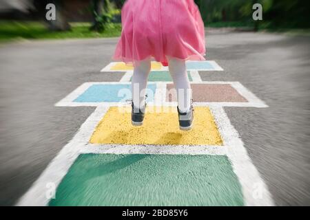 Nahaufnahme der Beine des Mädchens in einem rosa Kleid und hopscotch auf Asphalt gezogen. Kind spielt Hopscotch auf Spielplatz im Freien an einem sonnigen Tag. Im Freien Stockfoto