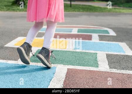 Nahaufnahme der Beine des Mädchens in einem rosa Kleid und hopscotch auf Asphalt gezogen. Kind spielt Hopscotch auf Spielplatz im Freien an einem sonnigen Tag. Im Freien Stockfoto