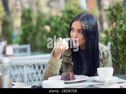 Nahaufnahme des Porträts einer jungen Frau, die Dessert Schokolade Eis leckt Löffel draußen in der Sommerterrasse Café. Seitenansicht Stockfoto