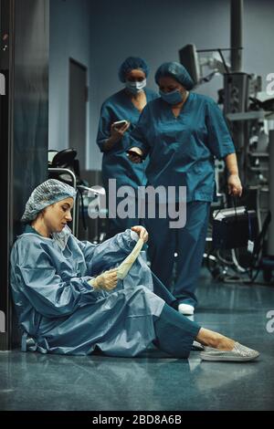 Müder Arzt sitzt nach der Operation im Krankenhausflur. Große Belastung für Ärzte und Medizin. Ruhe nach der Arbeit. Epidemie, Mangel an medizinischen Stockfoto