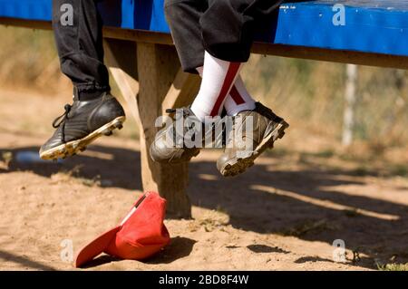 Beine von 2 Jungen auf der Bank eines Baseball Dugout sitzen Stockfoto