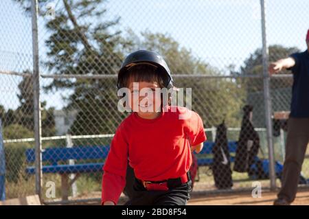 Junger Junge in Baseball-Helm mit großem Lächeln auf dem TBall-Feld Stockfoto