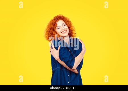 Liebe dich selbst Konzept. Closeup Portrait zuversichtlich lächelnde Frau mit umarmen sich isolierte gelbe Wand Hintergrund. Positive menschliche Emotion, Armaturenbrett Stockfoto