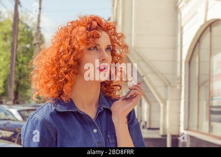 Sprecht mit meiner Hand. Verärgerte Frau mit roten lockigen Haaren, die das Handy in der Hand hält, ohne das Gespräch zu ignorieren, das frustriert draußen isoliert steht Stockfoto