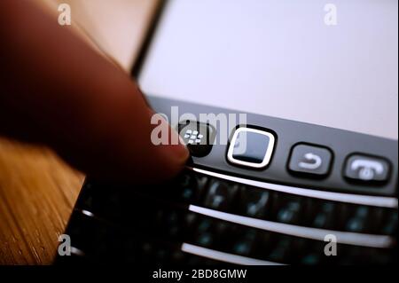 London, Großbritannien - 21. April 2013: Man Hand drückt die Home-Taste des BlackBerry RIM-Smartphones auf dem alten Smartphone-Telefon mit vollständiger qwerty-Tastatur Stockfoto