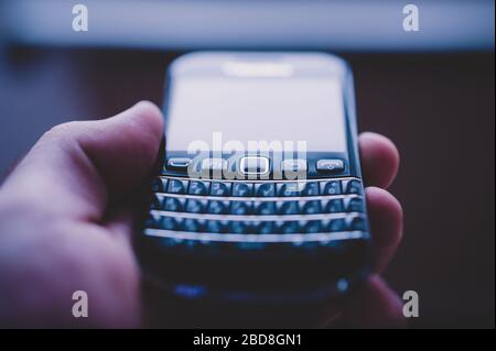 London, Großbritannien - 21. April 2013: Die männliche Hand hält das alte alte BlackBerry-Smartphonentelefon mit dem Fokus auf die erste Tastenreihe - das Tilt-Shift-Objektiv Stockfoto