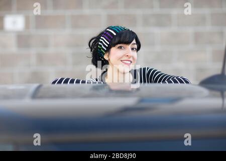 Junge Frau hinter einem Auto vor einem Gebäude Stockfoto