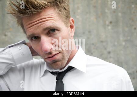 Porträt des ernsten Mannes in smart casual Outfit aus weißem Kleid Hemd und dünne Rückenbindung stehen im Freien vor einer strukturierten Betonwand Stockfoto