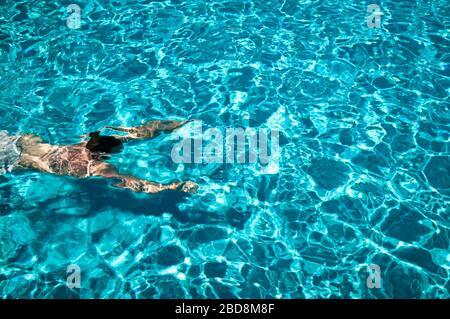 Blick von oben auf einen unerkennbaren Menschen, der unter Wasser in einem hellblauen Schwimmbad taucht Stockfoto