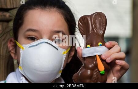 Coronavirus, Lexington, MA, USA. April 2020. Die 12-Jährige, die eine Gesichtsmaske trägt, hält ihr Schokoladenösterbündchen mit einer hausgemachten Gesichtsmaske. Credit: Chuck Nacke / Alamy Live News Stockfoto