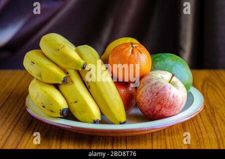 Frisches Obst, das auf einem Teller gestapelt ist, einschließlich Äpfel, Bananen, Mandarinorangen und Mango Stockfoto