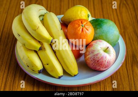 Frisches Obst, das auf einem Teller gestapelt ist, einschließlich Äpfel, Bananen, Mandarinorangen und Mango Stockfoto