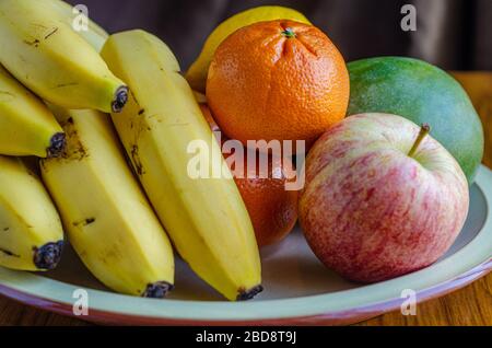 Frisches Obst, das auf einem Teller gestapelt ist, einschließlich Äpfel, Bananen, Mandarinorangen und Mango Stockfoto