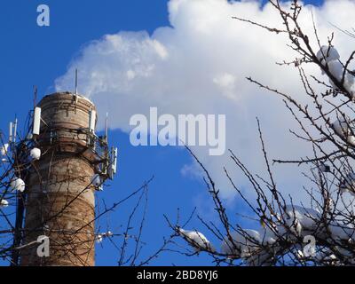 Rohre einer alten Fabrik werfen Wolken von giftigem weißem Rauch in den Himmel, die die Atmosphäre schädigen. Urbaner Smog aus Rauch aus Kesselhäusern. Weißer Rauch aus einem Kamin gegen einen blauen klaren Himmel. Stockfoto