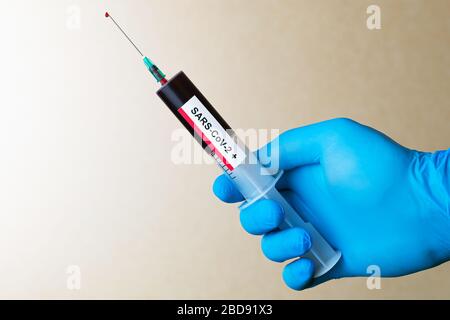 Die Ärzte halten die Spritze mit positivem Coronavirus Blut in Handschuhen. Ein Tropfen Blut auf der Spritzennadel. Selektiver Fokus. Stockfoto