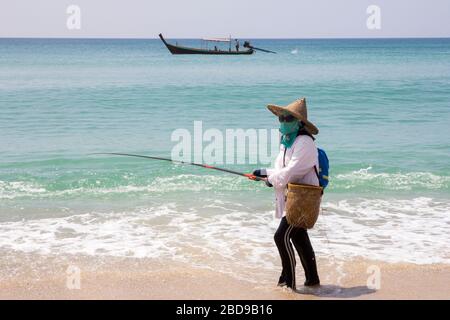 Phuket, Thailand-16. Oktober 2014: Eine Frau fischt vom Bang Tao Strand, wenn ein langes, verhülltes Boot vorbeiführt. Das Angeln ist ein Hauptstütze für einen Großteil des Phuket'schen Blocks Stockfoto