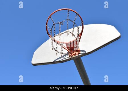 Blick auf einen alten Basketballkorb mit einem Metallkettennetz an einem sonnigen Frühlingstag. Stockfoto