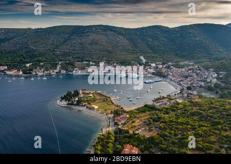 Luftaufnahme des Jachthafens Vis bei Sonnenuntergang, Kroatien, viele chaotisch stehende Boote in einer Bucht, Dächer von oranger Farbe, Sonnenschein, Hügel mit grünen Bäumen Stockfoto