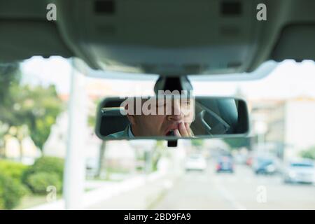 Rückspiegel Spiegelreflexion müde müde ermüdete gähnende erschöpfte junge britische Geschäftsleute, die nach langer Fahrstunde sein Auto im Verkehr fahren. Trans Stockfoto