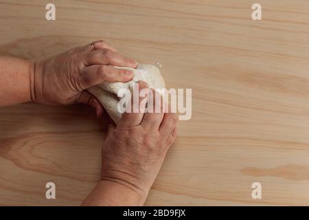 Blick von oben auf die Hände einer erwachsenen Frau, die Pizzateig in einem Holztisch in der Küche knetet Stockfoto