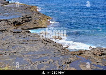 Blick auf eine Felsplattform oder ein Regal voller Rockpools und das Meer mit kleinen Wellen. Stockfoto