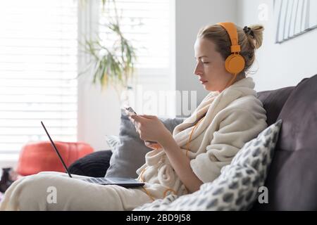 Soziale Distanzierung. Bleiben Sie zu Hause. Frau im bademantel ist bequem auf ihrem Sofa zu Hause und verwendet Social-Media-Apps auf dem Telefon für Videochats und Stying Stockfoto