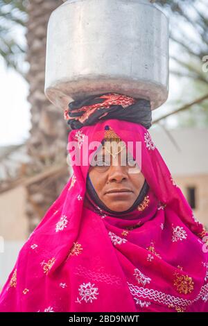 Eine omanische Frau im traditionellen Kleid, die eine Milchurne in einem Dorf im Sultanat Oman trägt. Stockfoto