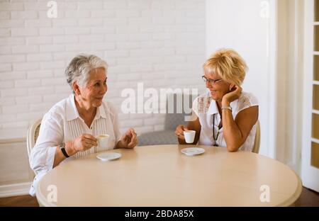 Ältere Mutter und reife alte Tochter sprechen und trinken Kaffee im Zimmer Stockfoto