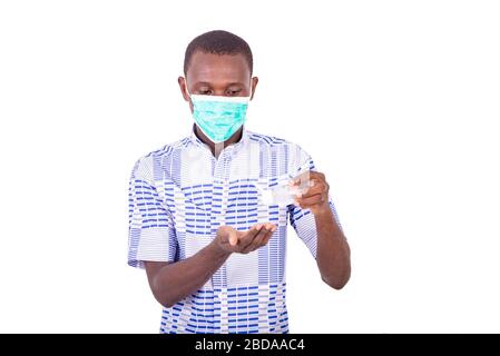 Junger Mann, der eine medizinische Maske trägt und eine Flasche antibakterielles Gel zum Händewaschen hält. Stockfoto