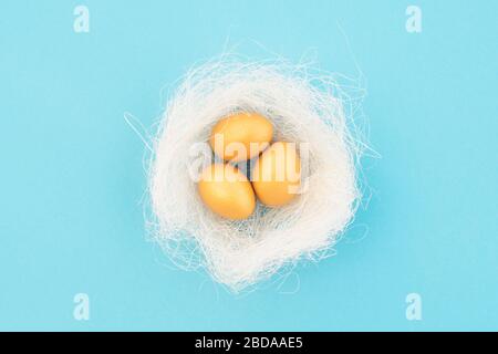 Dekoratives Vogelnest mit goldenen ostereiern auf blauem Pastellgrund. Osterkonzept. Flaches Lay. Stockfoto