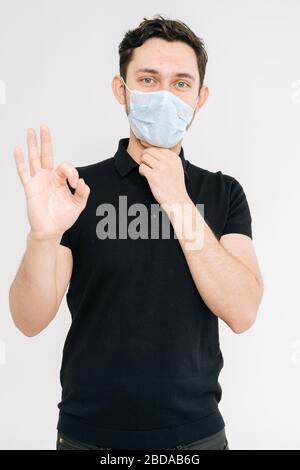 Kaukasischer junger Mann in medizinischer Maske und schwarzem T-Shirt mit OK-Schild Stockfoto