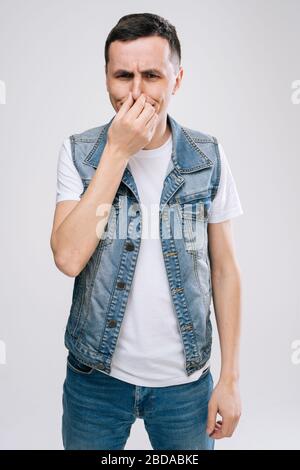 Studioaufnahme eines angeekelten kaukasischen jungen Mannes, der seine Nase hält, um schlechten Geruch zu vermeiden Stockfoto