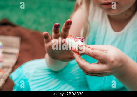 Süßes kleines Mädchen malt Osterei mit dem Finger, beschnitten Nahaufnahme mit gezieltem Fokus auf das Ei. Stockfoto