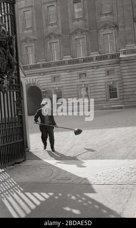 1960er, historisch, Buckingham Palace, London, Tore geöffnet und männliche Arbeiter in Anzug, Pullover und Mütze, mit Pinsel in der Hand, Westminster, London, England, Großbritannien. Stockfoto