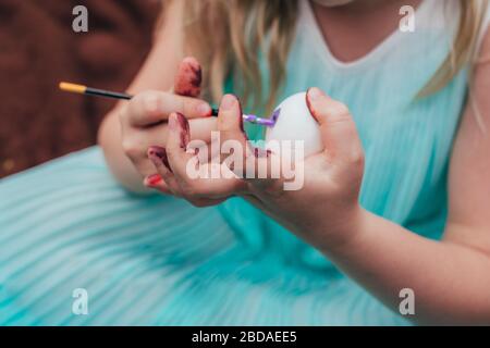 Süßes kleines Mädchen malt Osterei mit Pinsel, zugeschnittenes Nahfoto mit gezieltem Fokus auf das Ei. Stockfoto