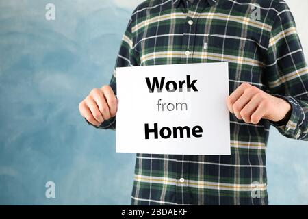 Mann hält Blatt mit Arbeit von zu Hause auf blauem Hintergrund. Quarantänekonzept Stockfoto