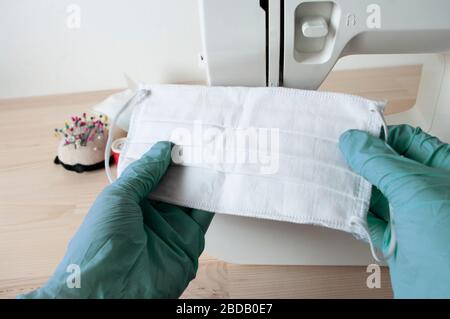 Hände grüne Handschuhe halten Maske. Maschine hinter nähen.Schützen Sie sich vor Coronavirus, Nähen medizinische Gesichtsmaske Stockfoto