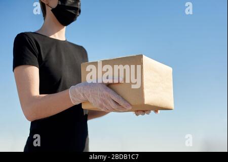 Der Lieferer in Gummihandschuhen und medizinischer Maske hält ein Paket in den Händen. Lieferservice in Quarantäne. Die Wirkung der Kovid-19-Pandemie. Stockfoto