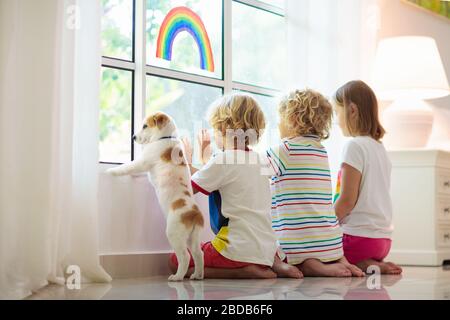Quarantäne des Coronavirus. Bleiben Sie zu Hause. Kinder sitzen am Fenster. Kinder, die ein Zeichen der Hoffnung auf Regenbogenfarben zeichnen. Junge und Mädchen während des Corona-Virus-Lockdowns. Kind und Stockfoto