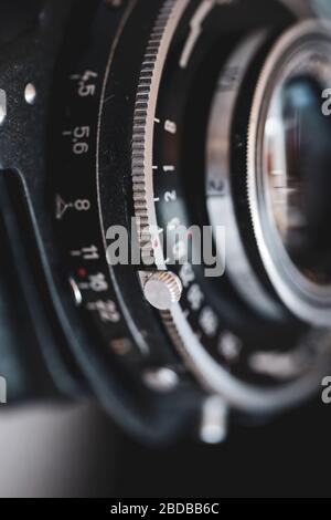 Makro- und geringe Schärfentiefe (selektiver Fokus) mit den Markierungen auf der Linse einer sehr alten Bälgenfotokamera (Belichtungszeit und Blendenstufen). Stockfoto