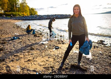 Junge Frau putzt Strand mit Freiwilligen bei Sonnenuntergang Stockfoto