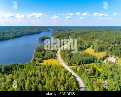 Luftaufnahme der Straße zwischen grünem Sommerwald und blauem See in Finnland Stockfoto