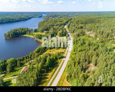 Luftaufnahme der Straße zwischen grünem Sommerwald und blauem See in Finnland Stockfoto