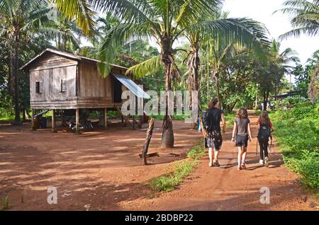 Eine Familie von Touristen geht an einem Stelzenhaus im Dorf Chi Phat, Cardamom Mountains, Kambodscha Stockfoto