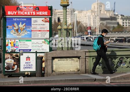 London, London, Großbritannien. April 2020. Eine Person, die eine Gesichtsmaske trägt, läuft am 7. April 2020 an einem geschlossenen Kiosk an der Westminster Bridge in London, Großbritannien vorbei. Kredit: Tim Ireland/Xinhua/Alamy Live News Stockfoto